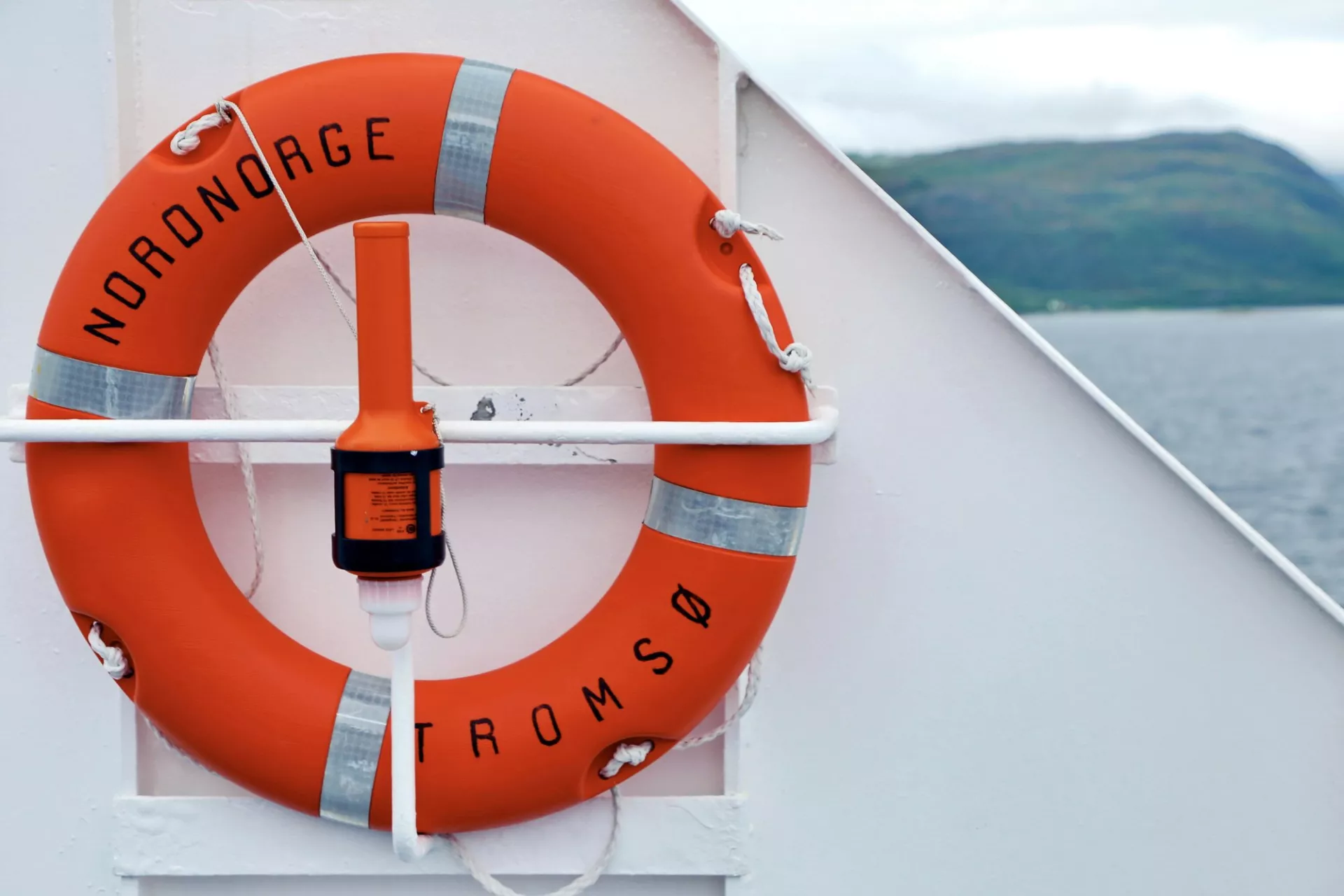An orange life buoy is mounted on the side of a ship.