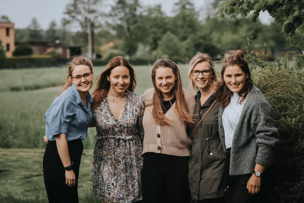 A group of five women standing outdoors, smiling, and posing for a photo.