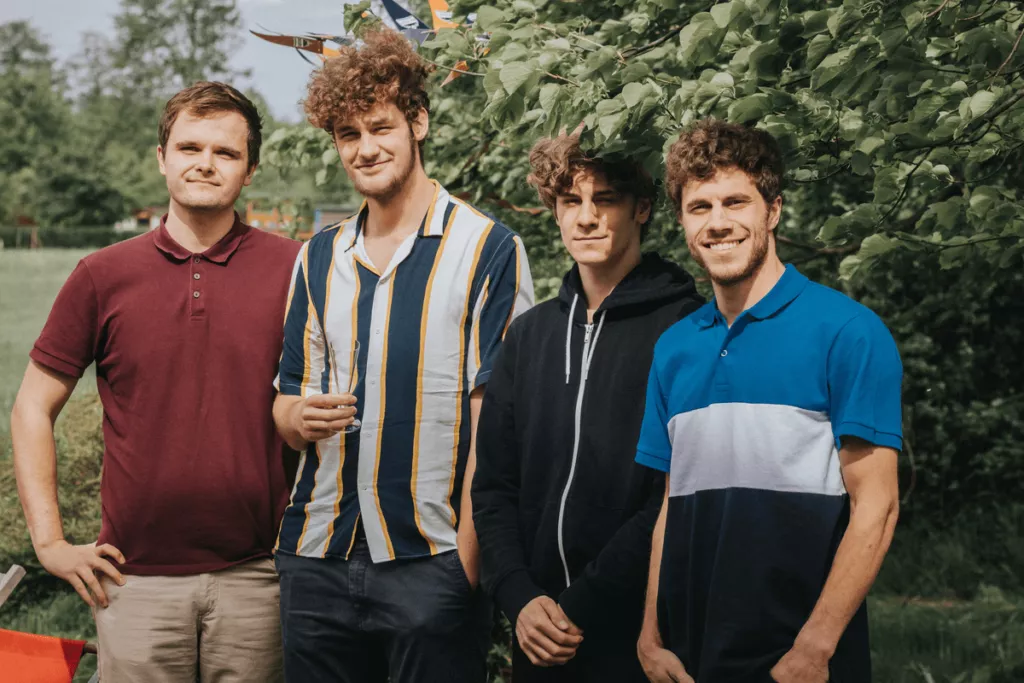 A group of four young men standing outdoors, smiling and posing for the camera.