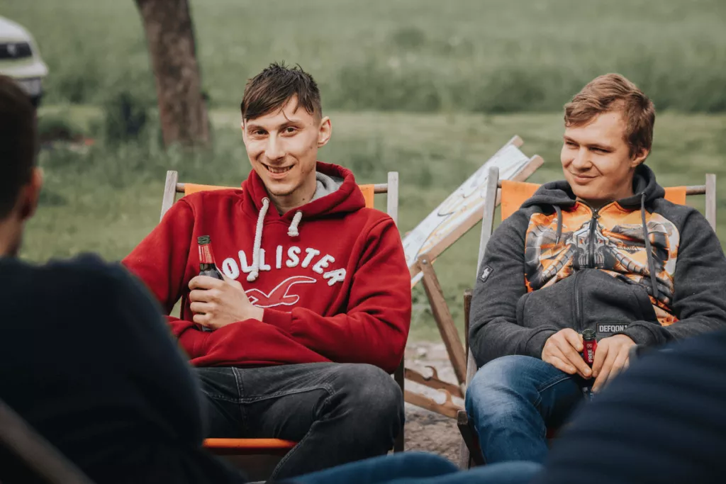Two young men, sitting in outdoor chairs, enjoying drinks and smiling